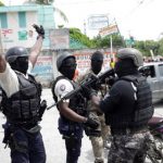 Manifestantes con uniformes de policía levantan sus brazos mientras se enfrentan a un oficial de la Policía Nacional Haitiana (PNH) de turno que sostiene un rifle durante una protesta organizada por el grupo radical "Fantom 509" en las calles de Puerto Príncipe, Haití, el 14 de septiembre de 2020. (REUTERS/Andrés Martínez Casares)