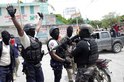 Manifestantes con uniformes de policía levantan sus brazos mientras se enfrentan a un oficial de la Policía Nacional Haitiana (PNH) de turno que sostiene un rifle durante una protesta organizada por el grupo radical "Fantom 509" en las calles de Puerto Príncipe, Haití, el 14 de septiembre de 2020. (REUTERS/Andrés Martínez Casares)