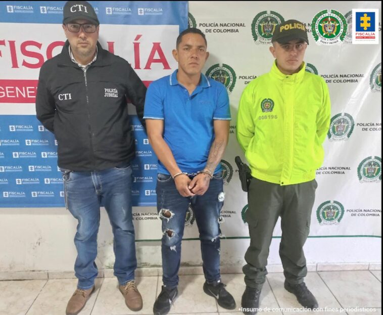 En la fotografía aparece Luis Eduardo Tapasco López junto a funcionarios del Cuerpo Técnico de Investigación (CTI) y la Policía Nacional y detrás tiene dos banner, uno con logos de la Policía y el otro de la Fiscalía.