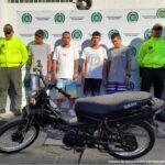En la foto aparecen cuatro presuntos integrantes de ‘Los Chatarreros’, acompañados a sus lados de dos uniformados de la Policía Nacional. Delante de ellos se ve una motocicleta incautada y detrás de ellos hay un pendón institucional de la Policía Nacional. 