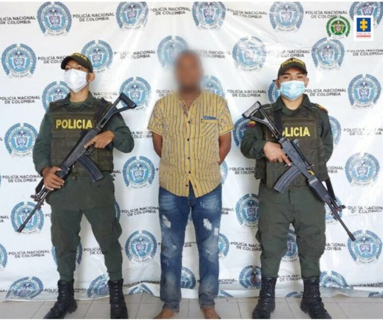 En la fotografía aparece un hombre capturado, junto a dos agentes de la Policía Nacional. En la parte posterior hay un banner de la misma institución.