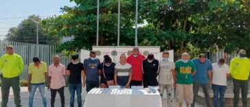 En la fotografía se observan a doce personas custodiadas por dos agentes de la Policía Nacional. Delante de ellos se encuentra una mesa blanca que muestra la droga que les fue incautada durante sus capturas.