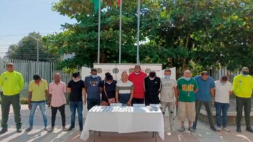 En la fotografía se observan a doce personas custodiadas por dos agentes de la Policía Nacional. Delante de ellos se encuentra una mesa blanca que muestra la droga que les fue incautada durante sus capturas.