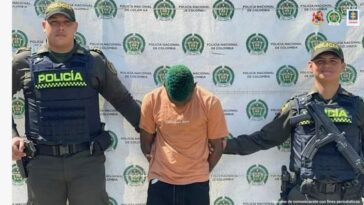 Jhon Alexánder Cordoba, alias Blanquito, aparece en la foto con dos policías a sus lados y un backing con logos de la Policia Nacional en la parte de atrás.