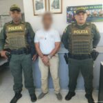 En la imagen se observa a un hombre con camiseta blanca y pantalón beis, custodiado por dos agentes de la Policía Nacional.