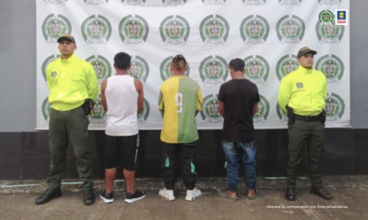 Están los tres capturados de espaldas custodiados por uniformados de la Policía Nacional. Detrás banner de la Policía.