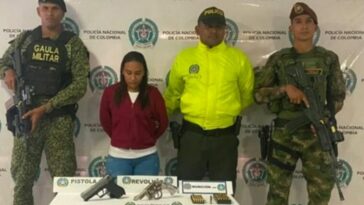 En la fotografía se observa a la capturada junto a un agente de la Policía a y a dos soldados del Gaula Militar. En la parte posterior se observa una mesa con dos armas de fuego, un proveedor y munición.