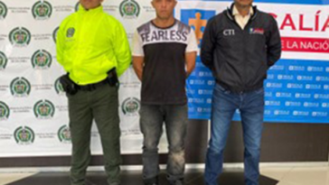 La imagen muestra al capturado junto a un investigador del CTI y un uniformado de la Policía Nacional. Detrás hay banners que identifican a la Policía Nacional y a la Fiscalía General de la Nación.