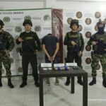 En la imagen se aprecia al capturado de espaldas junto a uniformados de la Policia y Ejército Nacional. Detrás de ellos banners que identifican al Departamento de Policía Arauca y Ejército Nacional.