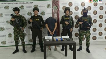 En la imagen se aprecia al capturado de espaldas junto a uniformados de la Policia y Ejército Nacional. Detrás de ellos banners que identifican al Departamento de Policía Arauca y Ejército Nacional.