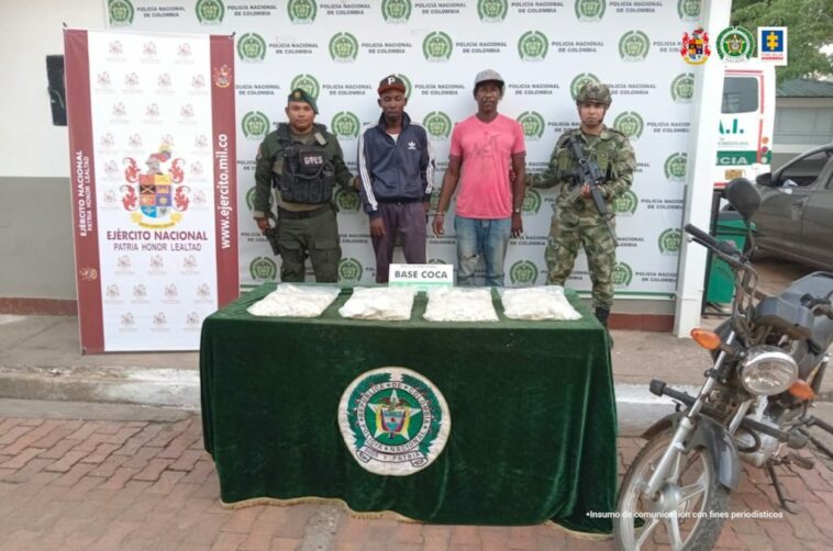 capturados custodiados por un militar y un policía, delante mesa con estupefacientes y moto incautados. Detrás banner de Policía y Ejército Nacional.